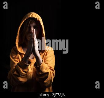 Eine Frau mit einer Kapuze auf dem Kopf betet auf schwarzem Hintergrund. Vorderansicht. Stockfoto