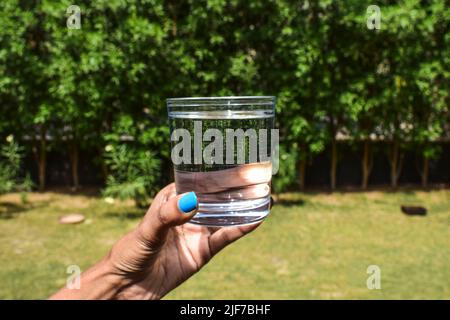 Junge Frau mit einem transparenten Glas voll mit frischem Mineralwasser in einer Hand mit Outdoor-Natur Hintergrund während der Sommersaison gefüllt Stockfoto