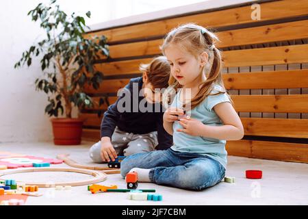 Kleines Mädchen und Junge sitzen auf dem Boden und spielen mit Bauherrin lego im Kindergarten. Kinder spielen Spiele mit Spielzeug im Spielzimmer. Interessant Stockfoto