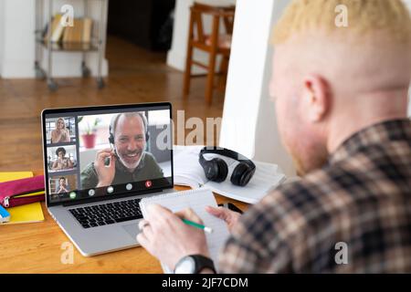 afroamerikanischer Albino-Mann macht sich Notizen, während er mit Kollegen zu Hause Videokonferenzen hält Stockfoto