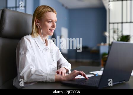 Frau sitzt vor ihrem Laptop und schaut lächelnd auf den Bildschirm. Stockfoto