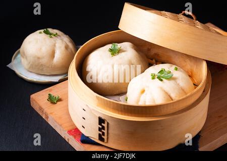 Asiatisches Speisekonzept Chinesischer Fleischknödel Baozi in Dim Sum Bambusdampfer auf Holzbrett auf schwarzem Schieferstein Hintergrund mit Kopierraum Stockfoto