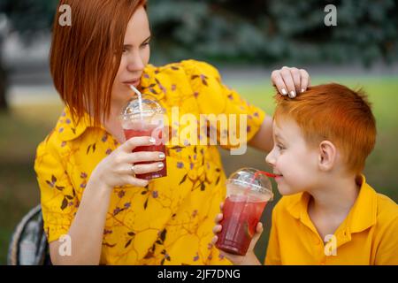 Der rothaarige junge Junge und die Mutter trinken rote Limonade. Sommer Erholung im Freien. Stockfoto