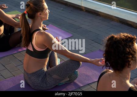 Multiethnische junge Frauen meditieren bei einem Yoga-Kurs bei Sonnenaufgang im Freien. Stockfoto