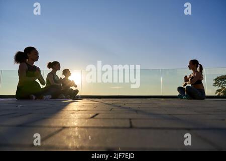 Verschiedene weibliche Silhouetten und Yogalehrerin, die im Freien meditiert. Stockfoto