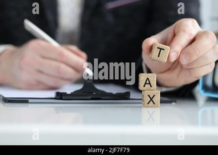 Hand hält Holzwürfelblock mit Text TAX Stockfoto