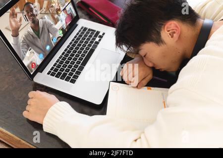 Gelangweilte asiatische Teenager schlafen vor dem Laptop während Online-Vortrag auf dem Tisch zu Hause Stockfoto