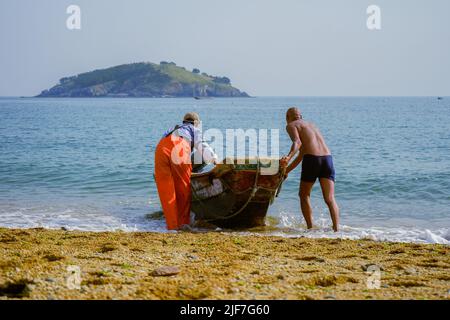 Die Fischer schieben das Boot vor dem Hintergrund einer kleinen Insel in Richtung Meer. Stockfoto