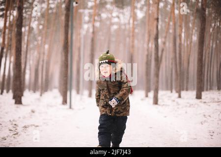 Glücklicher Junge, der im Winter im Park läuft Stockfoto