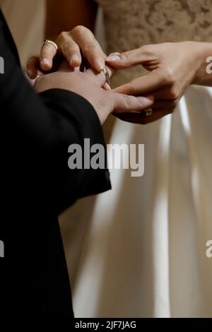 Details der Hände von Mann und Frau, die bei der Hochzeitszeremonie einen Ehering aufsetzen Stockfoto