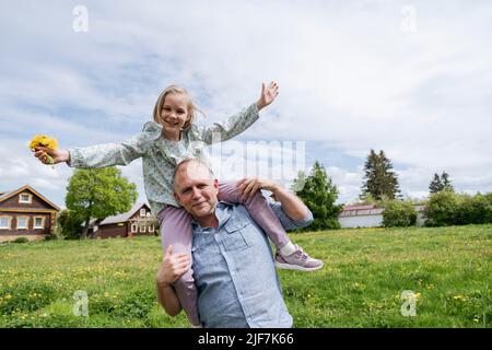 Das Mädchen sitzt auf den Schultern ihres Vaters und lacht. Stockfoto