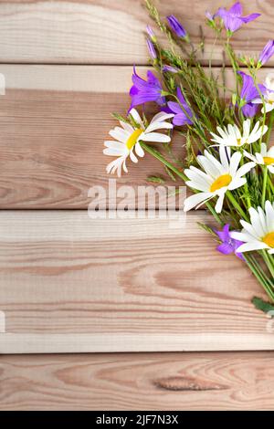 Blumen aus Blauhells und Gänseblümchen auf hellem Holzhintergrund in Form eines Straußes. Herzlichen Glückwunsch. Urlaub. Geburtstag. Ein flacher Kopierbereich mit einem t Stockfoto