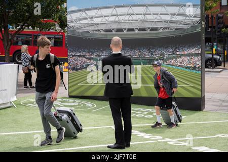 Ein Bild des Centre Court der Lawn Tennis Association befindet sich vor dem Bahnhof Wimbledon, wo die Öffentlichkeit während der zweiwöchigen Meisterschaften am 30.. Juni 2022 in London, England, vorbeiläuft. Stockfoto