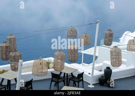 Santorini, Griechenland - 13. Mai 2021 : Blick auf eine malerische Terrasse mit Tischen, Stühlen und Lichtern mit Blick auf die Ägäis Stockfoto