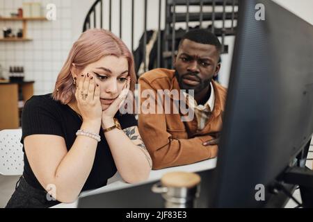 Besorgte Geschäftsfrau und Geschäftsmann, die im Büro einen Computermonitor angeschaut haben Stockfoto