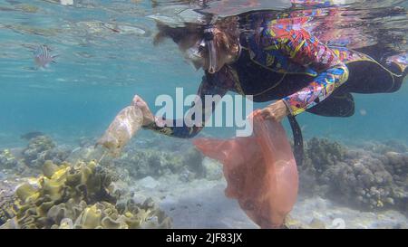 Frau in Tauchausrüstung schwimmt und sammelt Plastikmüll unter Wasser auf dem Boden des Korallenriffs. Schnorchler reinigt Ozean von Plastikverschmutzung. P Stockfoto