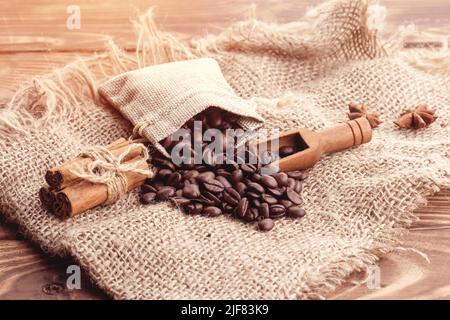 Kaffeebohnen im Beutel, Zimt und Anis auf dem hölzernen Hintergrund Kaffee ist die gute Idee Stockfoto