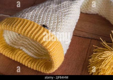 Detailansicht eines wunderschönen Wintermütze-Designs von einer lateinischen Kunsthandwerkerin zu Hause. Handgestrickter Hut mit Häkeltechnik auf einem orangefarbenen Holzhintergrund Stockfoto