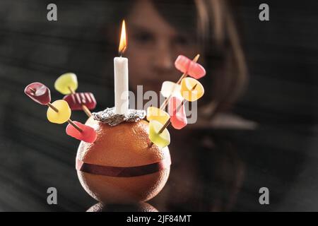 Ein kleines Mädchen schaut sich den Orange Christingle an, den sie gemacht hat. Selektiver Fokus. Stockfoto