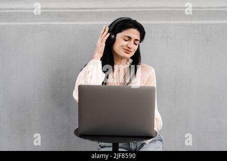 Attraktive dj-Frau mit Laptop und Kopfhörern, die Musik mischt und neue Kompositionen hört. Adorable georgischen Mädchen genießen ihr Leben mit Musik hören Stockfoto