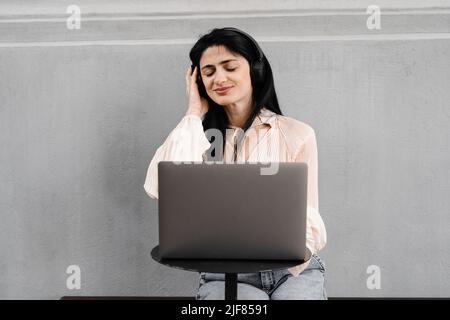 Attraktive dj-Frau mit Laptop und Kopfhörern, die Musik mischt und neue Kompositionen hört. Adorable georgischen Mädchen genießen ihr Leben mit Musik hören Stockfoto