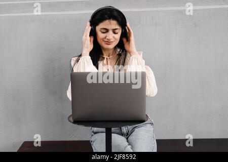 Attraktive dj-Frau mit Laptop und Kopfhörern, die Musik mischt und neue Kompositionen hört. Adorable georgischen Mädchen genießen ihr Leben mit Musik hören Stockfoto