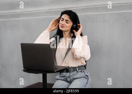 Attraktive dj-Frau mit Laptop und Kopfhörern, die Musik mischt und neue Kompositionen hört. Adorable georgischen Mädchen genießen ihr Leben mit Musik hören Stockfoto