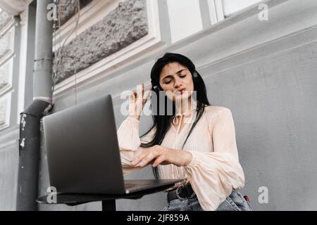 Attraktive dj-Frau mit Laptop und Kopfhörern, die Musik mischt und neue Kompositionen hört. Adorable georgischen Mädchen genießen ihr Leben mit Musik hören Stockfoto