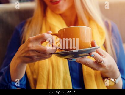 Frau in einer blauen Bluse und einem gelben Schal, die Kaffee im Café trinkt. Denken Sie an die Ukraine Stockfoto