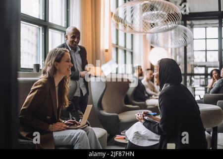 Fröhlicher junger Geschäftsmann mit Hijab, der mit einem Kollegen im Kreativbüro spricht Stockfoto