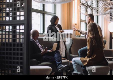 Männliche und weibliche Unternehmer diskutieren über Laptop von Kollegen im Kreativbüro Stockfoto