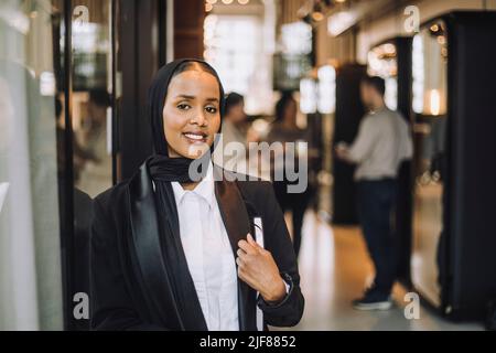 Lächelnder junger Unternehmer mit Kopftuch und Tagebuch im Büro Stockfoto