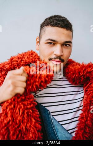 Porträt eines schwulen Mannes, der eine rote Pelzjacke an der Wand trägt Stockfoto