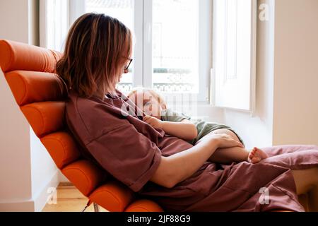 Mutter mit Sohn sitzt zu Hause auf einem Stuhl Stockfoto