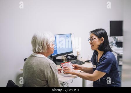 Reife Ärztin diskutiert über Pille Organisator mit älteren Patienten im Krankenhaus Stockfoto