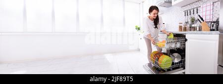 Lächelnden jungen Frau, die die Platten in der Spülmaschine zu Hause Stockfoto