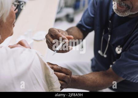 Männlicher Arzt injiziert ältere weibliche Patienten in der medizinischen Klinik Stockfoto