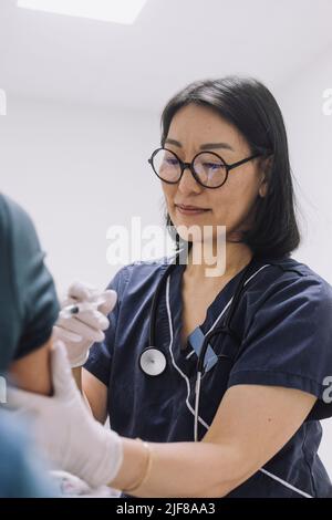 Ärztin mit Brillen, die den Patienten im Krankenhaus injiziert Stockfoto