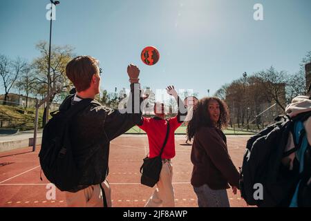 Männer spielen mit Ball, während sie mit Freunden auf dem Sportplatz an sonnigen Tagen spazieren gehen Stockfoto