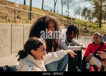 Glückliche multirassische männliche und weibliche Freunde sprechen, während sie im Park sitzen Stockfoto