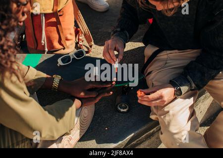 Mittelteil eines Mannes, der Fingernägel einer Freundin malte, die in der Nähe des Skateboards sitzt Stockfoto