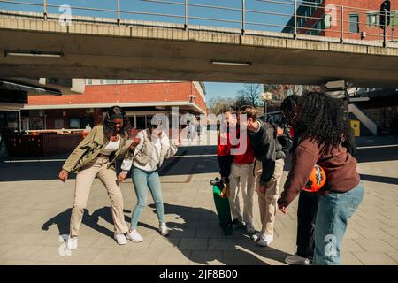 Multirassische Freunde beobachten junge Frauen, die an sonnigen Tagen auf der Straße tanzen Stockfoto