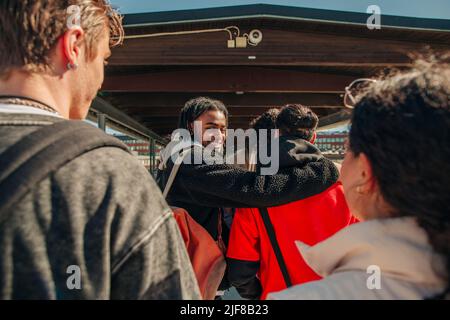 Lächelnder junger Mann, der über die Schulter blickt, während er mit Freunden am Bahnhof läuft Stockfoto