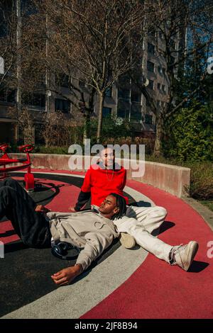 Mann, der sich am sonnigen Tag auf dem Schoß eines männlichen Freundes auf dem Spielplatz entspannt Stockfoto