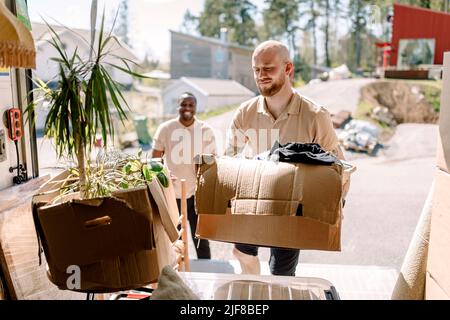 Multirassische Mover, die an sonnigen Tagen Kisten vom Lastwagen tragen Stockfoto