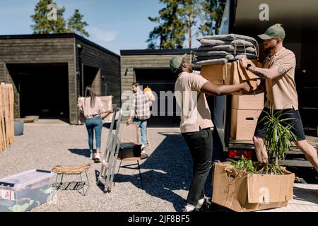 Multirassische Mover entladen Boxen aus LKW, während Paar im Hintergrund Stockfoto