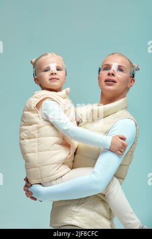 Virtuelle Technologie. Glücklich erfreut nettes Mädchen lächelnd und Blick auf die Kamera, während Mutter in ihren Armen in digitalen virtuellen Brille auf der Bienge hält Stockfoto