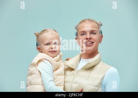 Virtuelle Technologie. Glücklich erfreut nettes Mädchen lächelnd und Blick auf die Kamera, während Mutter in ihren Armen in digitalen virtuellen Brille auf der Bienge hält Stockfoto