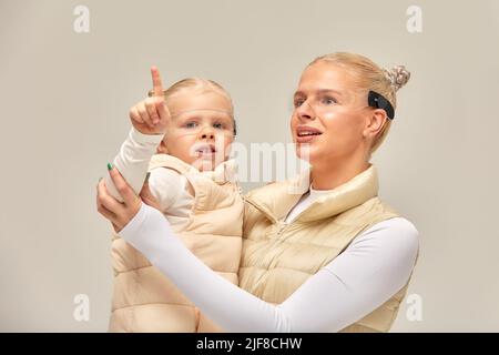 Virtuelle Technologie. Glücklich erfreut nettes Mädchen lächelnd und Blick auf die Kamera, während Mutter in ihren Armen in digitalen virtuellen Brille auf der Bienge hält Stockfoto