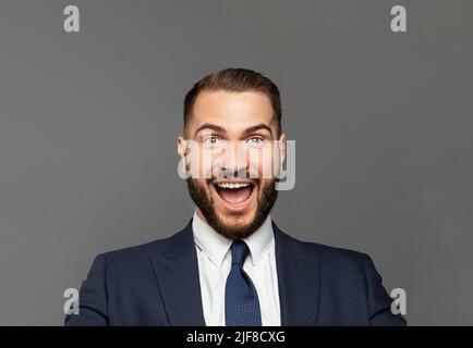 Junger glücklicher Geschäftsmann mit wirklich beeindruckenden Leistungen schreiend vor Glück, männliches Gesicht aus der Nähe Stockfoto